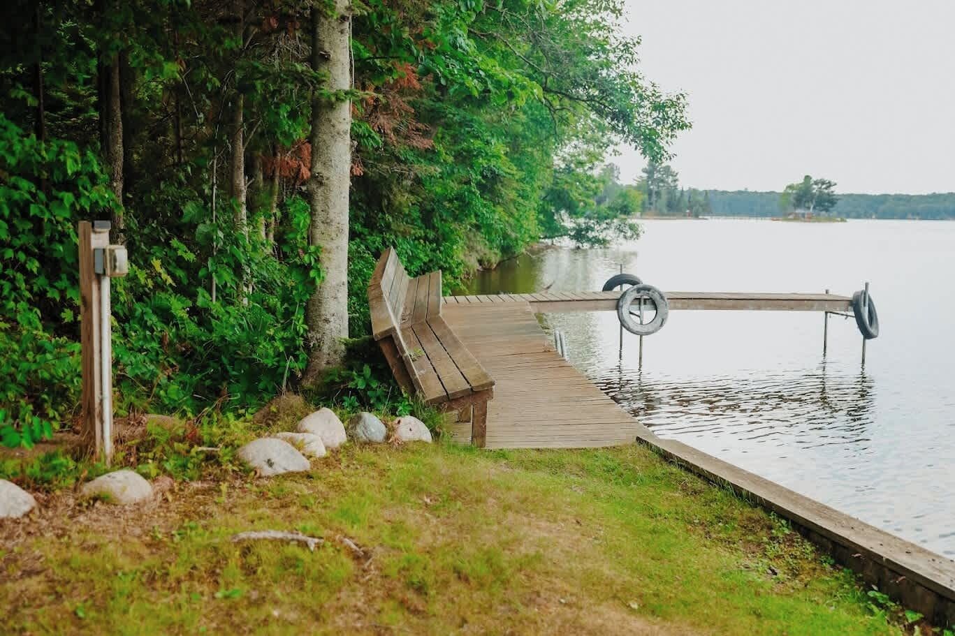 A wooden dock extending into a calm lake, surrounded by lush greenery and trees.