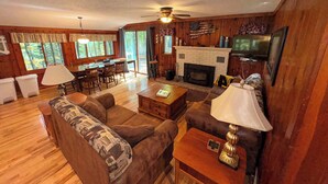 Ein gemütliches Blockhaushaus-Interieur mit Kamin, Holzwänden, einem Essbereich und einem Wohnzimmer mit Sofas und Couchtisch.