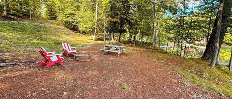 Un camping con dos sillas Adirondack rojas, una mesa de picnic y un pozo para hacer fuego.