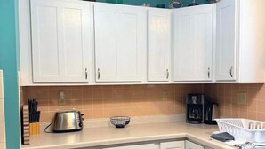 Een keuken met witte kastjes, een koffiezetapparaat en een waterkoker op het aanrecht.