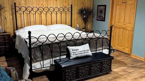 Een slaapkamer met een houten paneel hoofdbord, een bed met witte lakens, een zwarte metalen bank met kussen, en een houten deur met de tekst 'PRIVATE'.