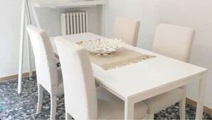 Ein weißer Esstisch mit vier Stühlen, einem dekorativen Mittelstück und einer weißen Stehlampe im Hintergrund.