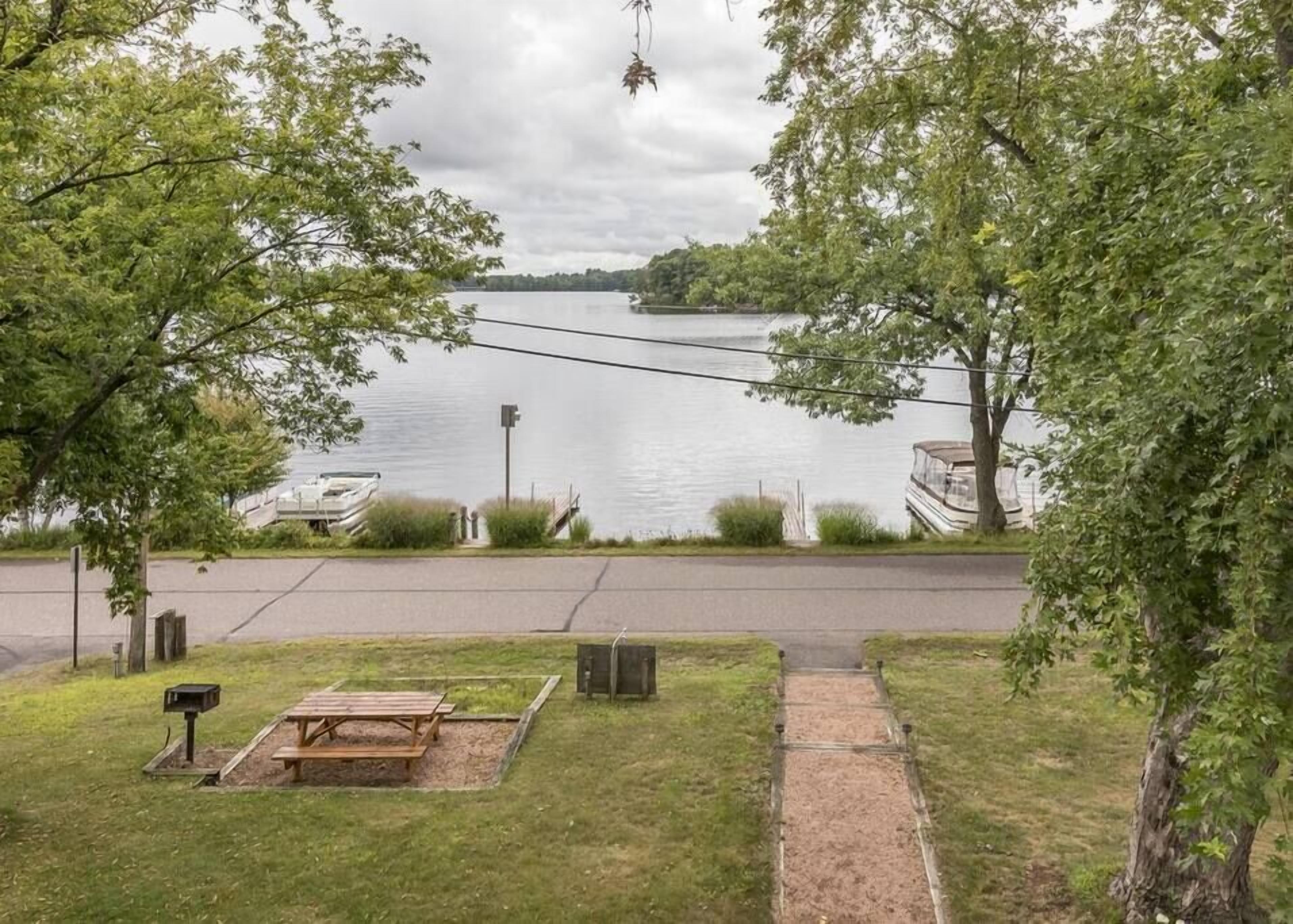 A lakeside view with picnic tables, a dock, and boats.