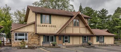 A two-story building with a sign reading "Island Cove." It features a stone facade, multiple windows with green shutters, and a parking lot in front.