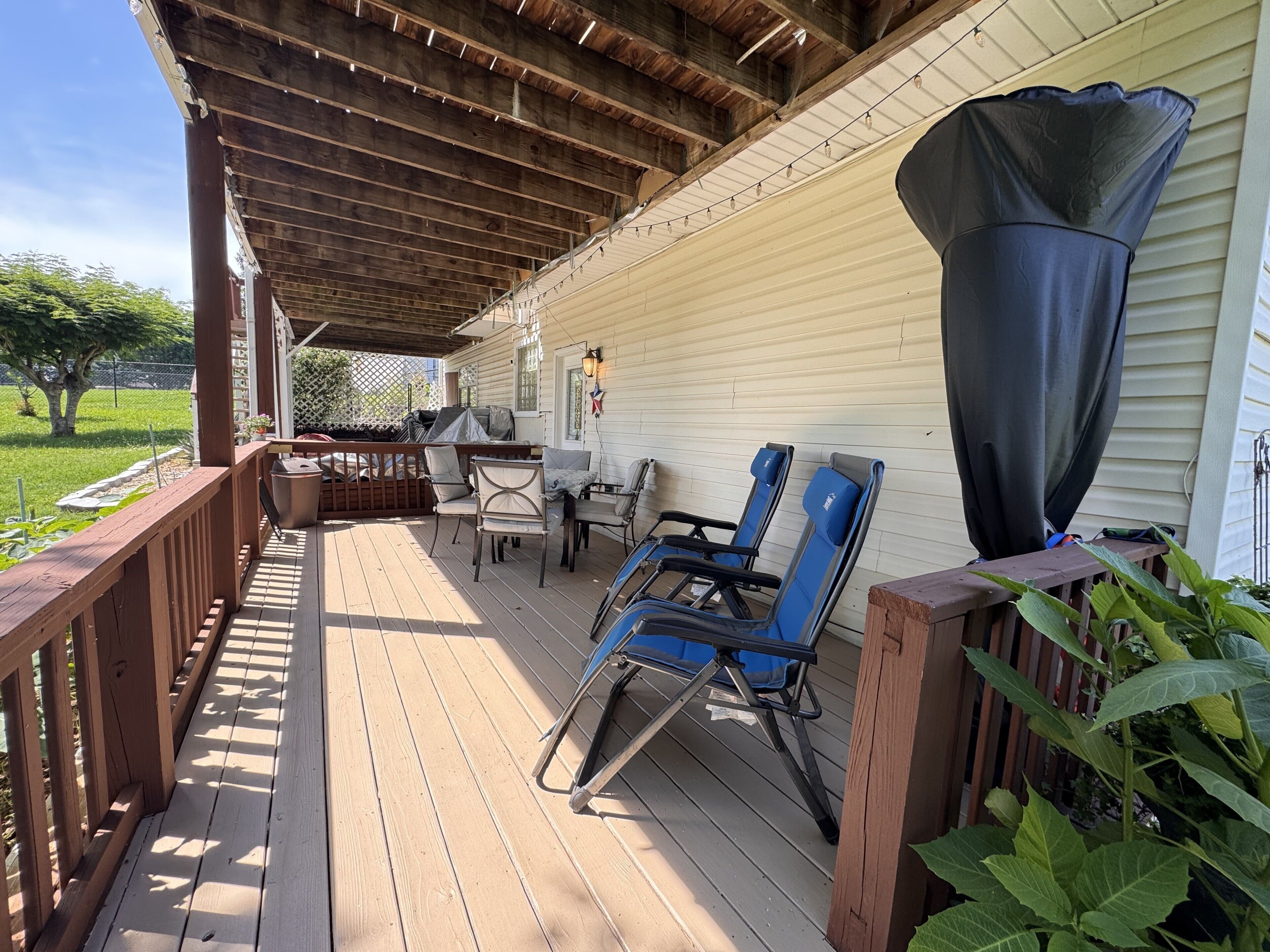 A covered outdoor deck with wooden railings, a table, chairs, and a grill.