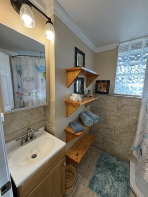 A bathroom with a white sink, wooden shelves, a mirror, and a shower curtain with a cityscape design. - Cozy 1-bedroom apartment in charming Flowery Branch with AC (Flowery Branch)