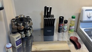 A kitchen counter with various cooking utensils, a cutting board, and containers of spices.
