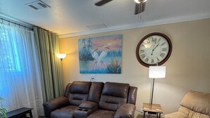 A living room with a reclining sofa, a coffee table, a lamp, a clock, and a painting on the wall.