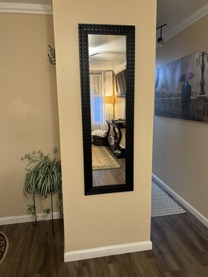 A mirror with a black frame reflecting a room with a bed, a lamp, and a window with curtains. - Cozy 1-bedroom apartment in charming Flowery Branch with AC (Flowery Branch)