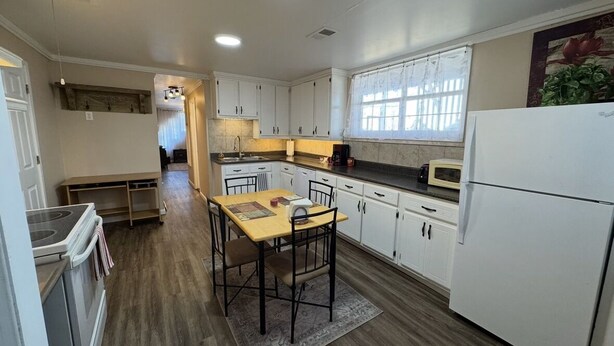 A kitchen with white cabinets, a wooden countertop, a refrigerator, and a dining area with a table and chairs.