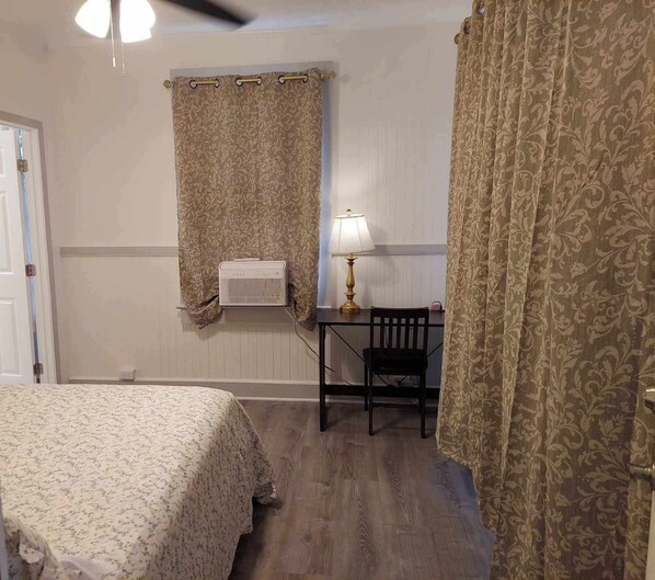 Ein Schlafzimmer mit zwei Betten, einem Schreibtisch mit Stuhl, einer Lampe und einem Fenster mit Vorhängen.