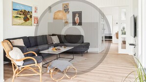 Ein modernes Wohnzimmer mit einem grauen Sofa, Korbstühlen, einem Couchtisch und Kunstwerken an den Wänden.