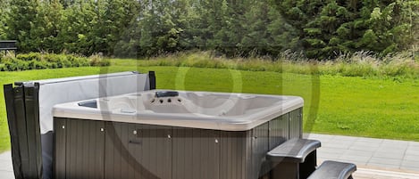 A hot tub with a wooden deck, surrounded by a grassy area and trees.