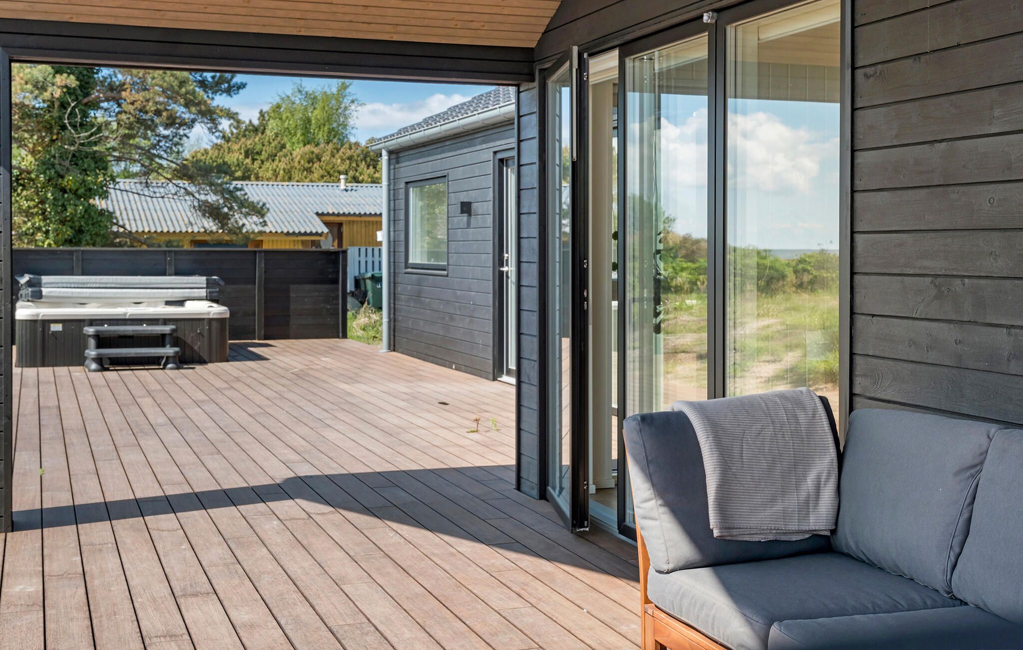 A covered outdoor deck with a barbecue, a sofa, and a sliding glass door leading to a house.