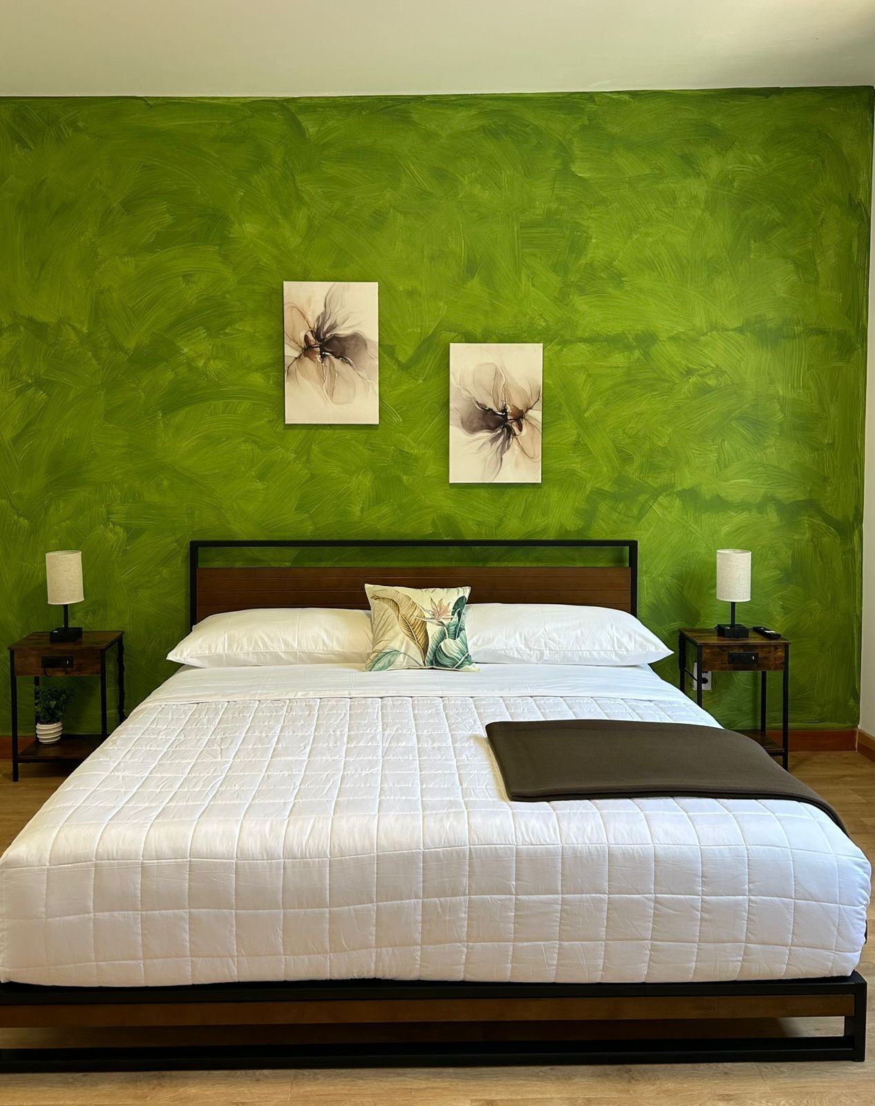 A bed with a white quilted bedspread, two pillows, a dark throw blanket, and two nightstands with lamps.