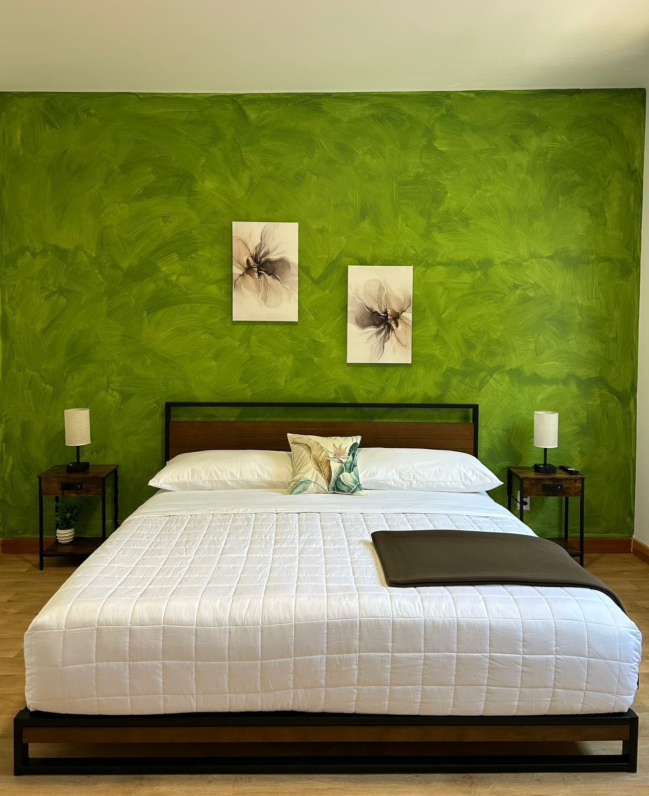 A bed with a white quilted bedspread, two pillows, a dark throw blanket, and two nightstands with lamps.