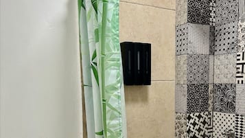 A bathroom with a bamboo shower curtain, a handheld showerhead, and patterned tiles.