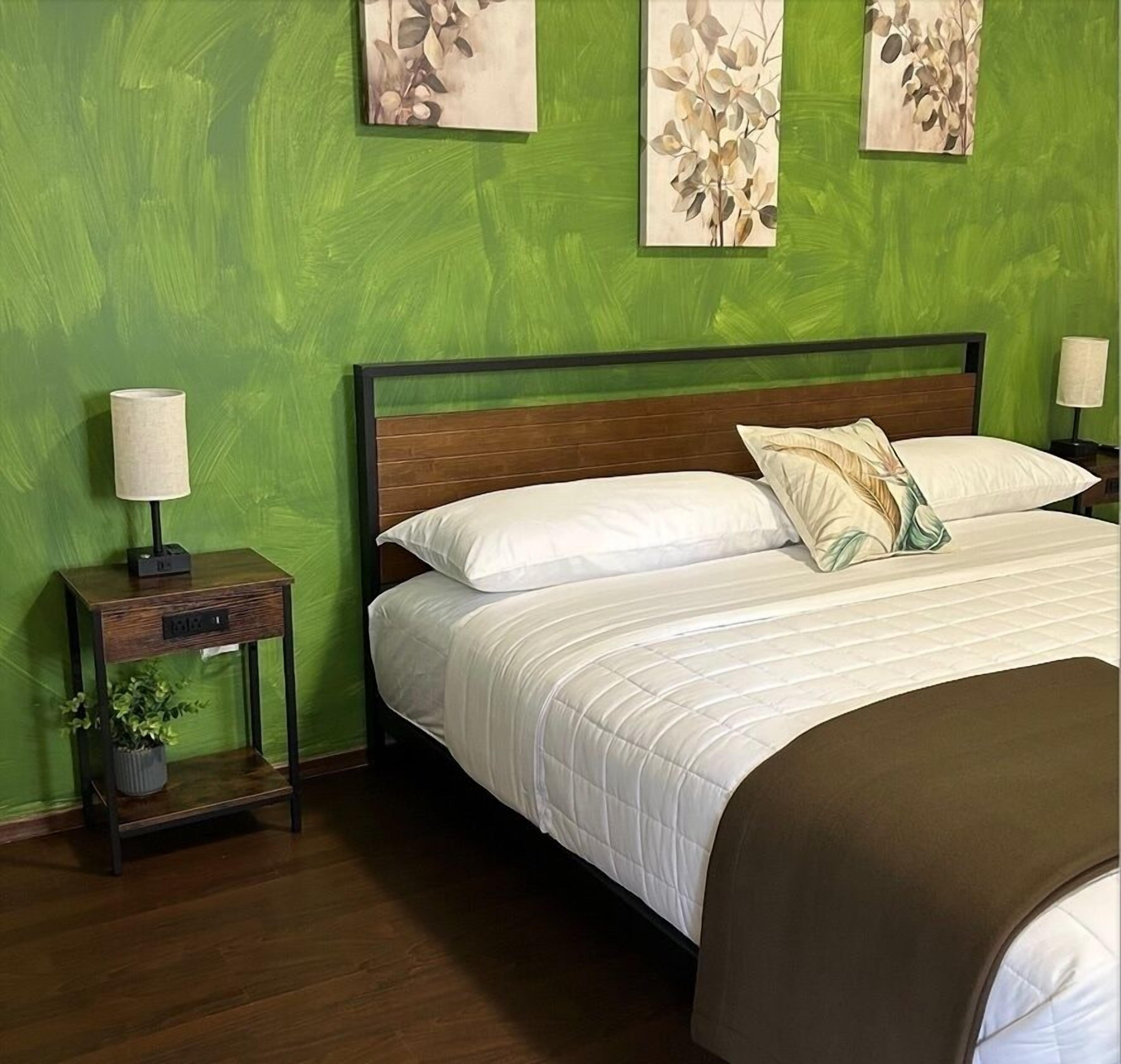 Un dormitorio con una cama, una mesita de noche con lámpara y un cuadro en la pared.