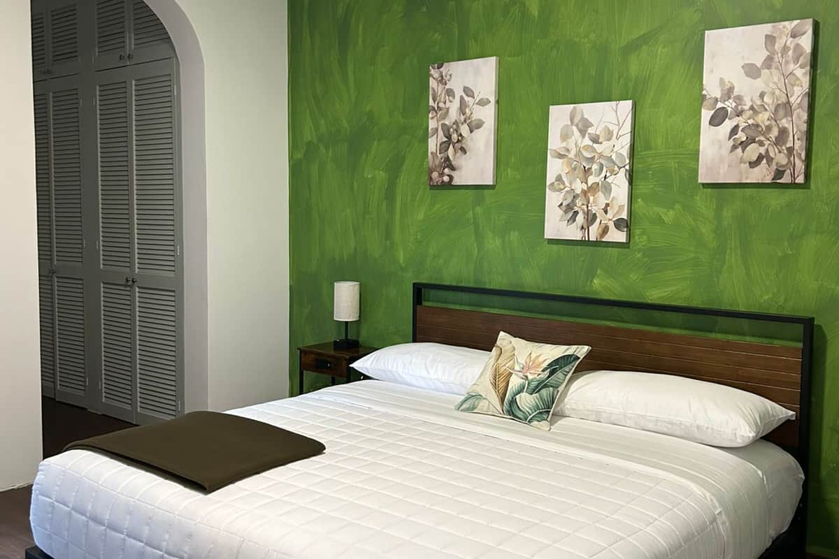 A bedroom with a green wall, a bed with white bedding, and two wall-mounted paintings.