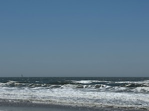 A beach with waves and a distant sailboat. - The Compass OKI: Beautiful Beach House on OKI, NC- 250 feet from access (Oak Island)