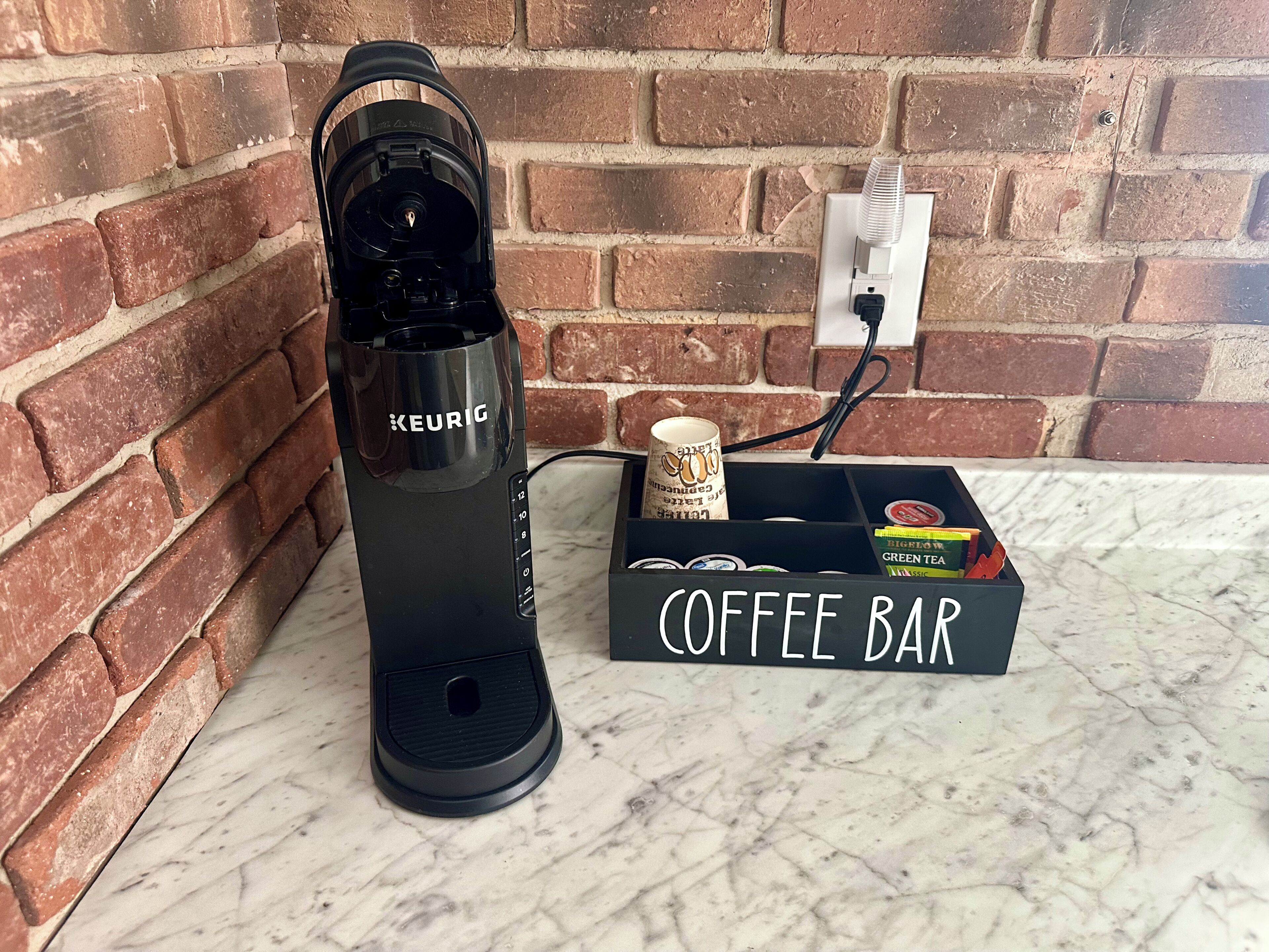 Eine schwarze Keurig-Kaffeemaschine neben einer Kaffeebar mit einer Tasse und einer Schachtel grüner Tee.
