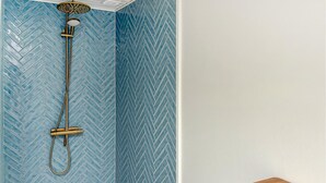 Ein Badezimmer mit blauer Wandverkleidung aus Fischgrätmuster, einer goldfarbenen Duschbrause und einer Holzbank.