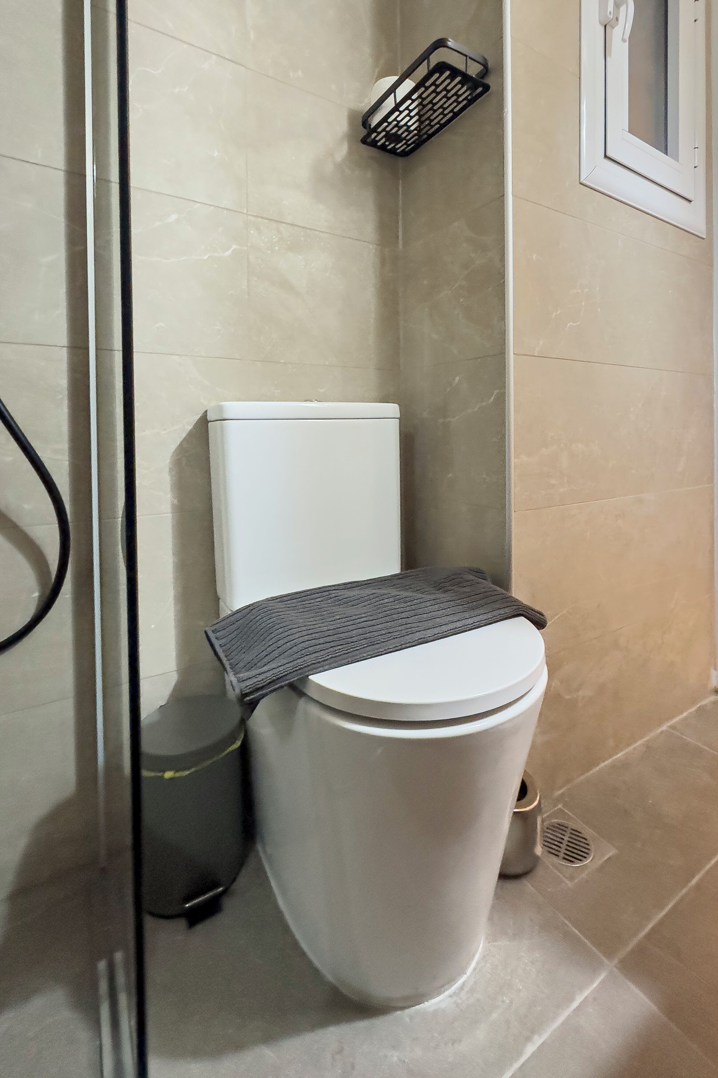 A bathroom with a white toilet, a black trash bin, and a shower area.