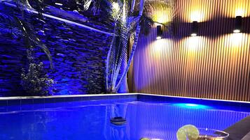 A poolside area with a pizza box, two drinks, and a tropical setting with palm trees and a stone wall.