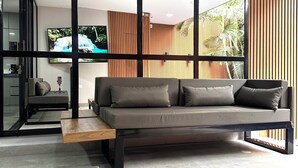 Een moderne woonkamer met een grijze bank, houten lambrisering en een groot raam met uitzicht op groen.