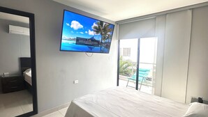 Een moderne slaapkamer met een groot bed, een flatscreen televisie aan de muur en een schuifdeur naar een balkon.