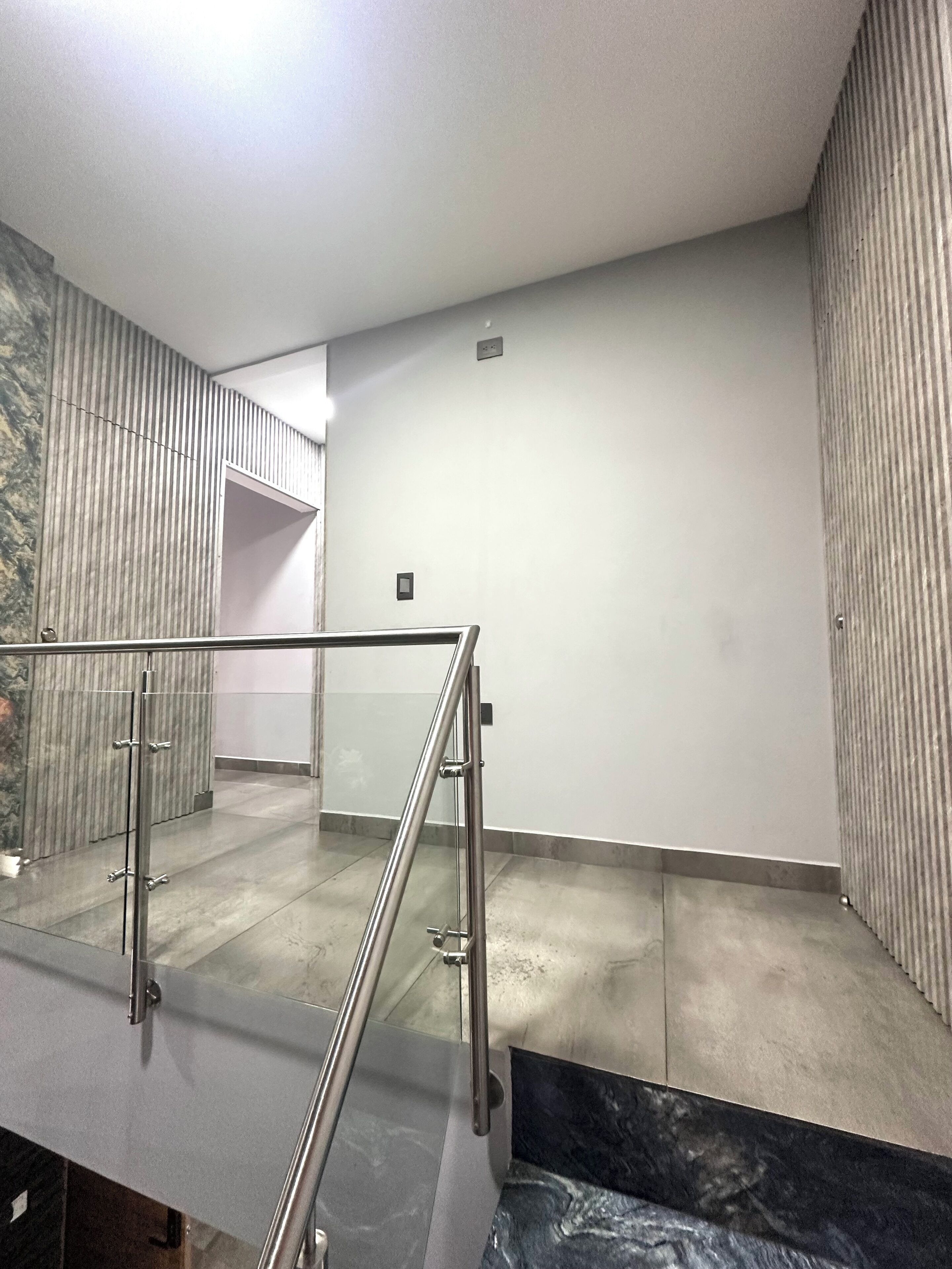 Een modern interieur met een glazen balustrade, een betegelde vloer en een effen wand met een kleintje ventilatierooster.
