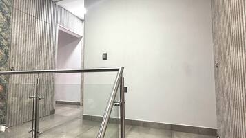 Een modern interieur met een glazen balustrade, een betegelde vloer en een effen wand met een kleintje ventilatierooster.