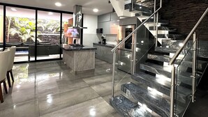 Een moderne keuken met een centraal eiland, een eetgedeelte met uitzicht, en een trap met glazen balustrades.