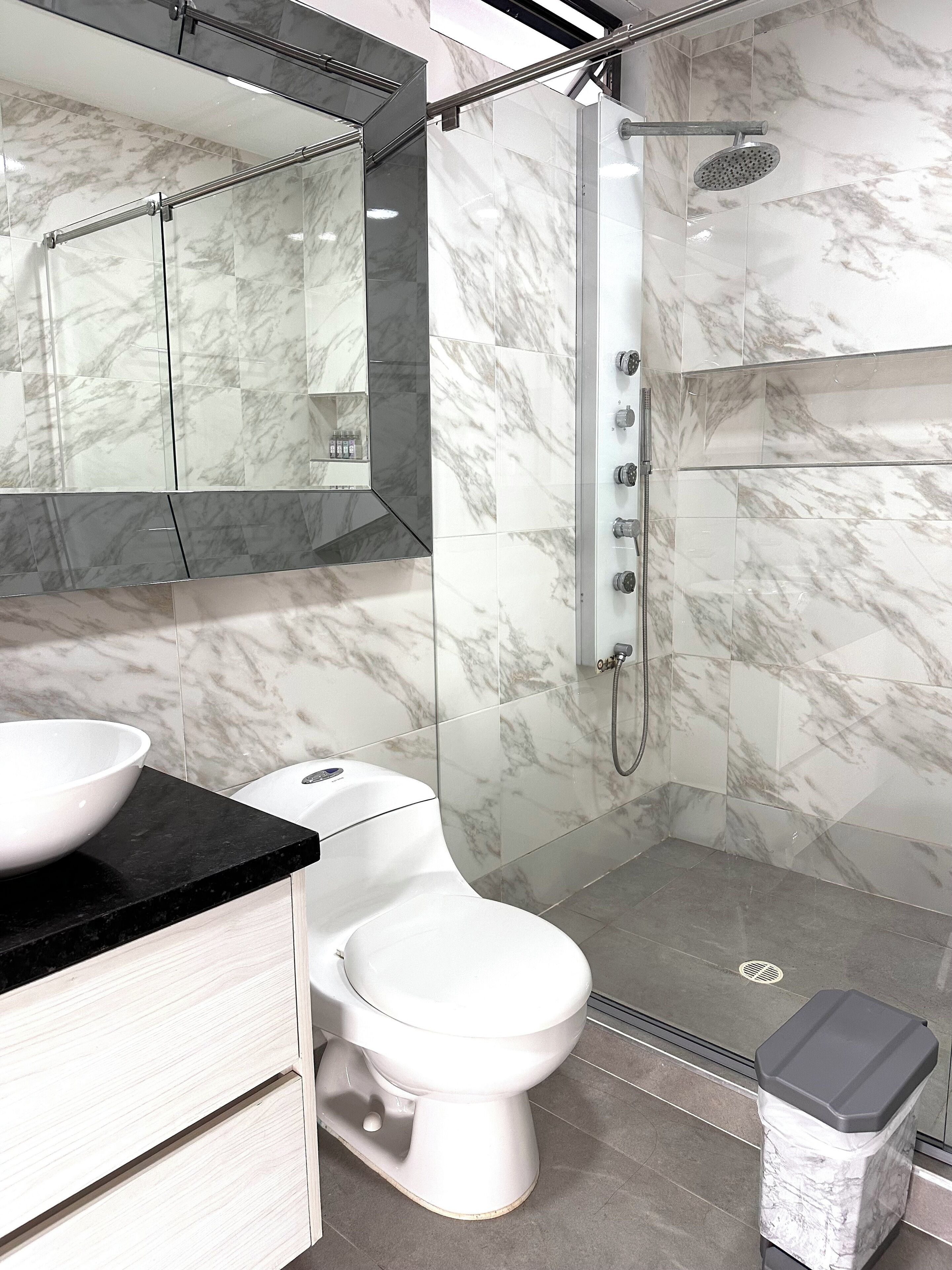 A modern bathroom with a marble shower, a white toilet, and a black countertop with a bowl.