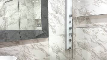 A modern bathroom with a marble shower, a white toilet, and a black countertop with a bowl.