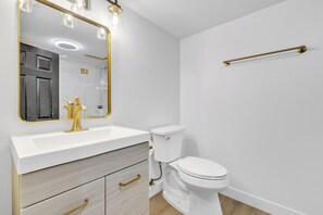 Une salle de bain moderne avec un lavabo blanc, des accessoires dorés et un grand miroir.