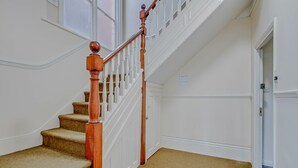 Een bekleed trappenhuis met houten spijlen en een witte leuning, dat leidt naar een deur met een klein kleedje aan de voet.