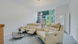 Een moderne woonkamer met twee beige leren fauteuils, een kleine ronde tafel en een groot raam met uitzicht op groen.