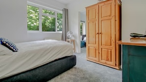 Een slaapkamer met een bed, een houten garderobe, een ventilator en een raam met uitzicht op bomen.