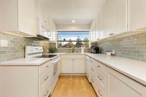 A modern kitchen with white cabinetry, a built-in oven, a dishwasher, and a window providing a view of the outdoors. - 3BR Seattle Home w/ Spacious Yard | Near Northgate (Seattle)