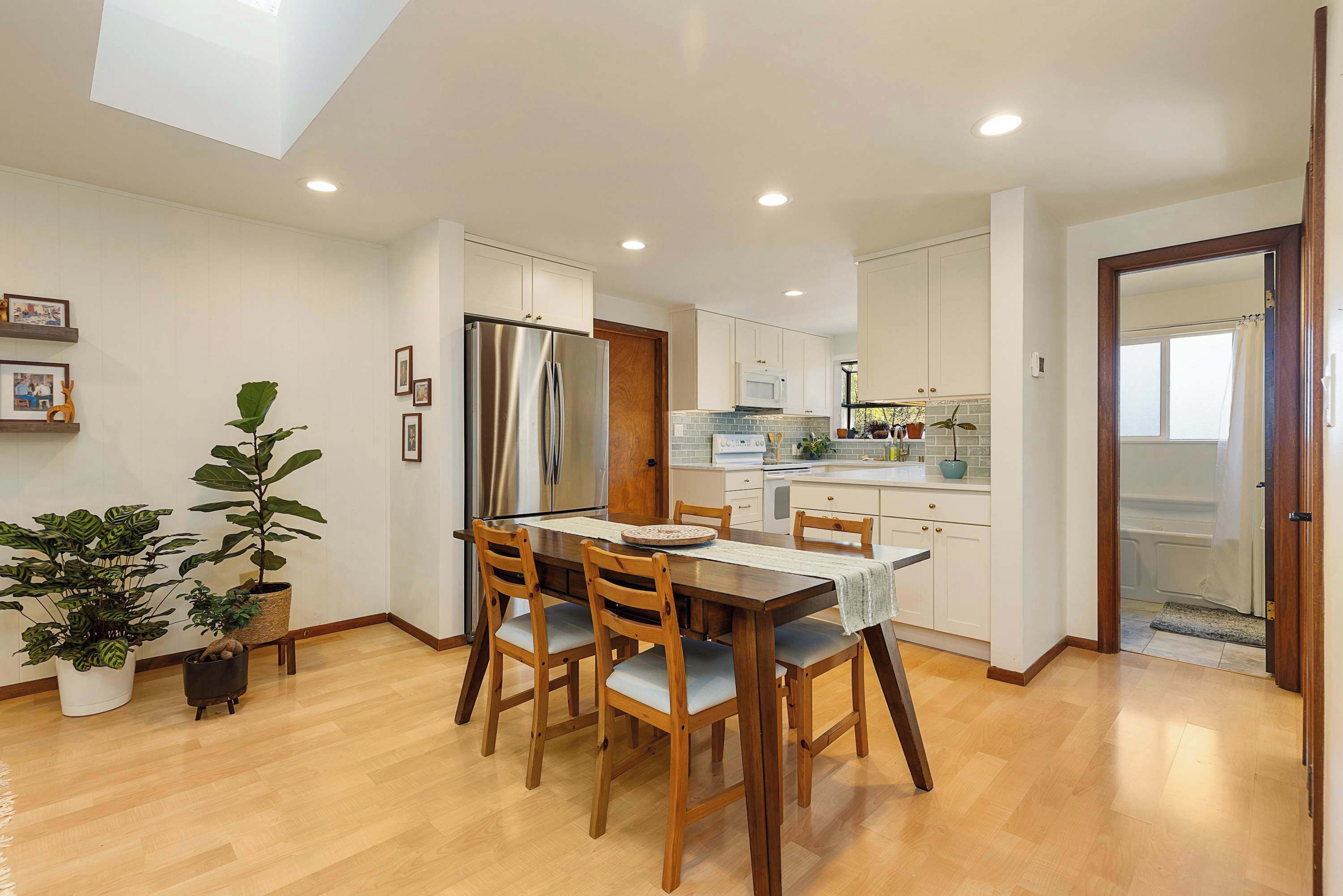 A modern kitchen with white cabinets, a stainless steel refrigerator, and a dining area with a wooden table and chairs.