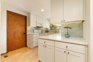 A kitchen with white cabinets, a microwave, a stove, and a sink. - 3BR Seattle Home w/ Spacious Yard | Near Northgate (Seattle)
