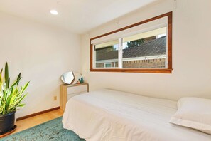 A bedroom with a single bed, a window with a view of a house, a bedside table with a mirror, and a potted plant. - 3BR Seattle Home w/ Spacious Yard | Near Northgate (Seattle)