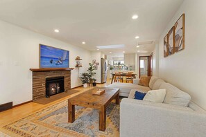 A living room with a fireplace, a sofa, a coffee table, and a painting on the wall. - 3BR Seattle Home w/ Spacious Yard | Near Northgate (Seattle)