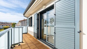A residential balcony with a tiled floor, a sliding glass door, and a white railing.