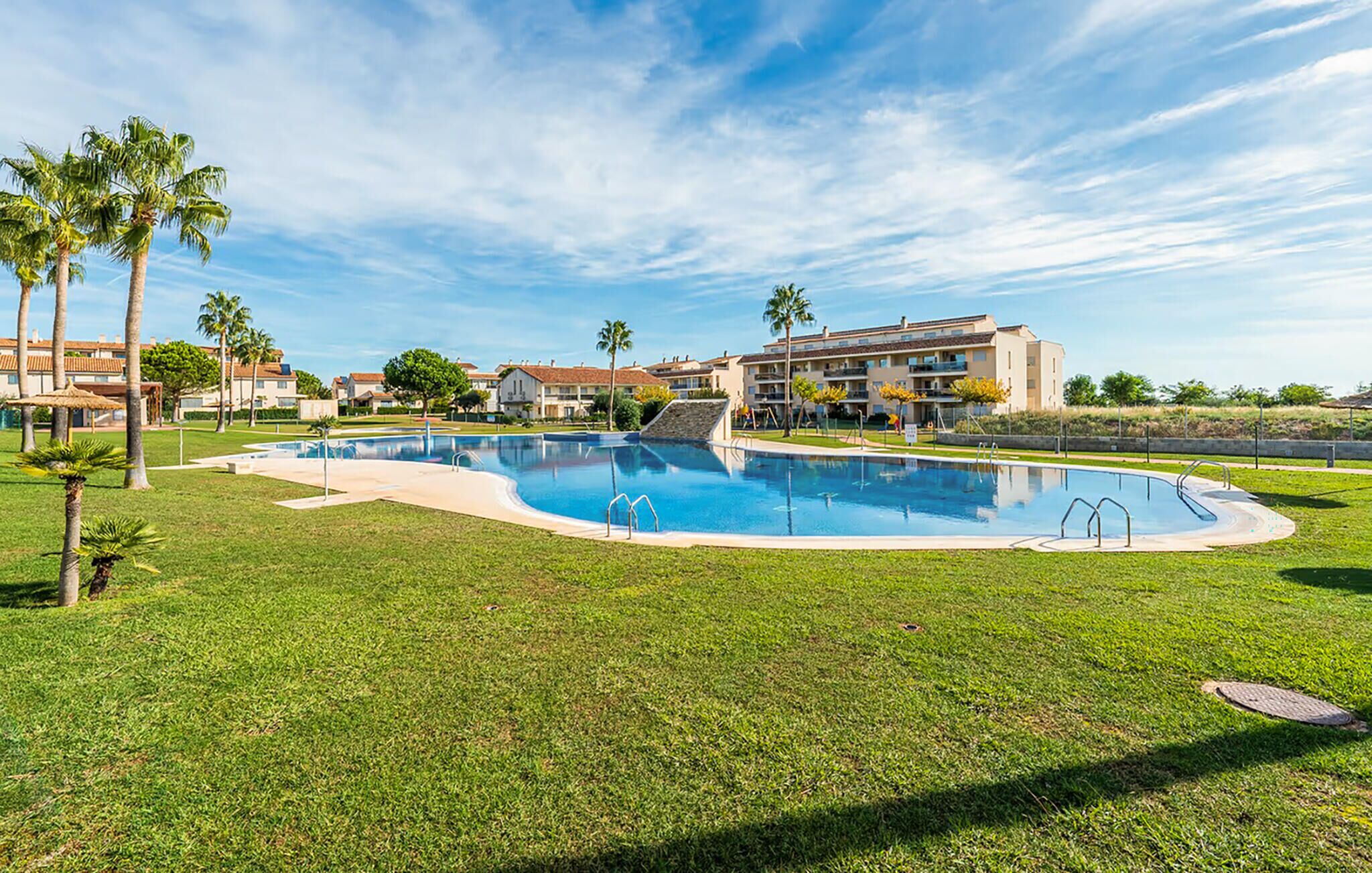 Ein Swimmingpool, umgeben von gepflegtem Rasen und Palmen, mit einem Gebäude im Hintergrund.