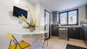 A modern kitchen with a glass table, yellow chairs, a flower vase, and a TV on the wall.