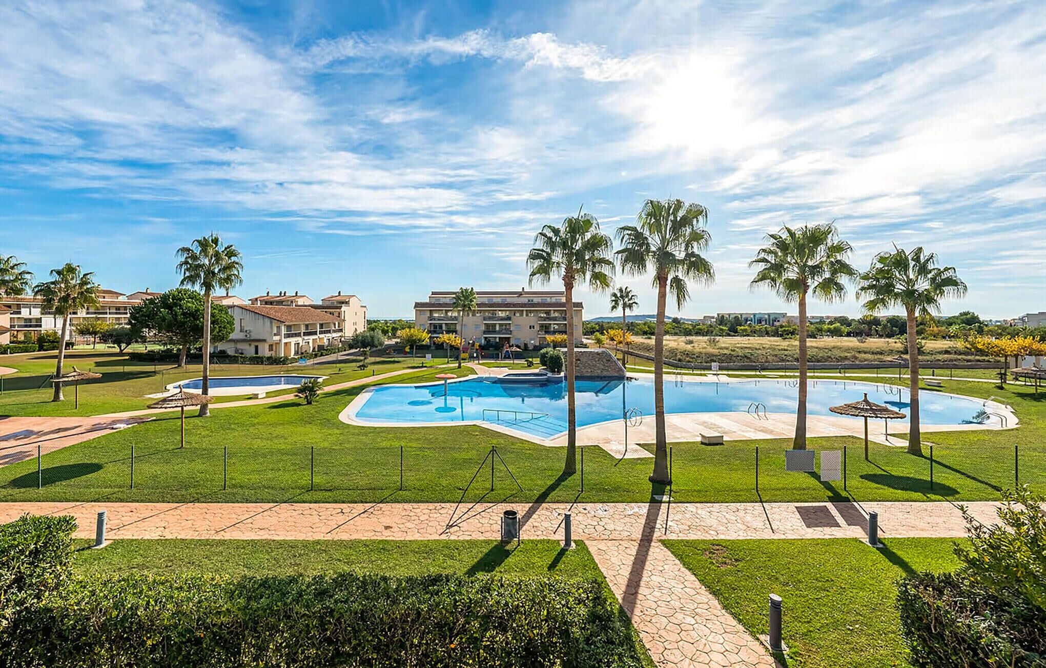 A resort with a large swimming pool, palm trees, and a clear blue sky.