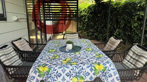 Une terrasse couverte avec une table et des chaises, une plante en pot et, au fond, un portique rouge.