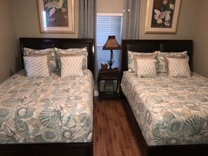A hotel room with two beds, each with patterned bedding and pillows, a bedside table with a lamp, and framed artwork on the walls. - Tropic Winds 905 (Panama City Beach)